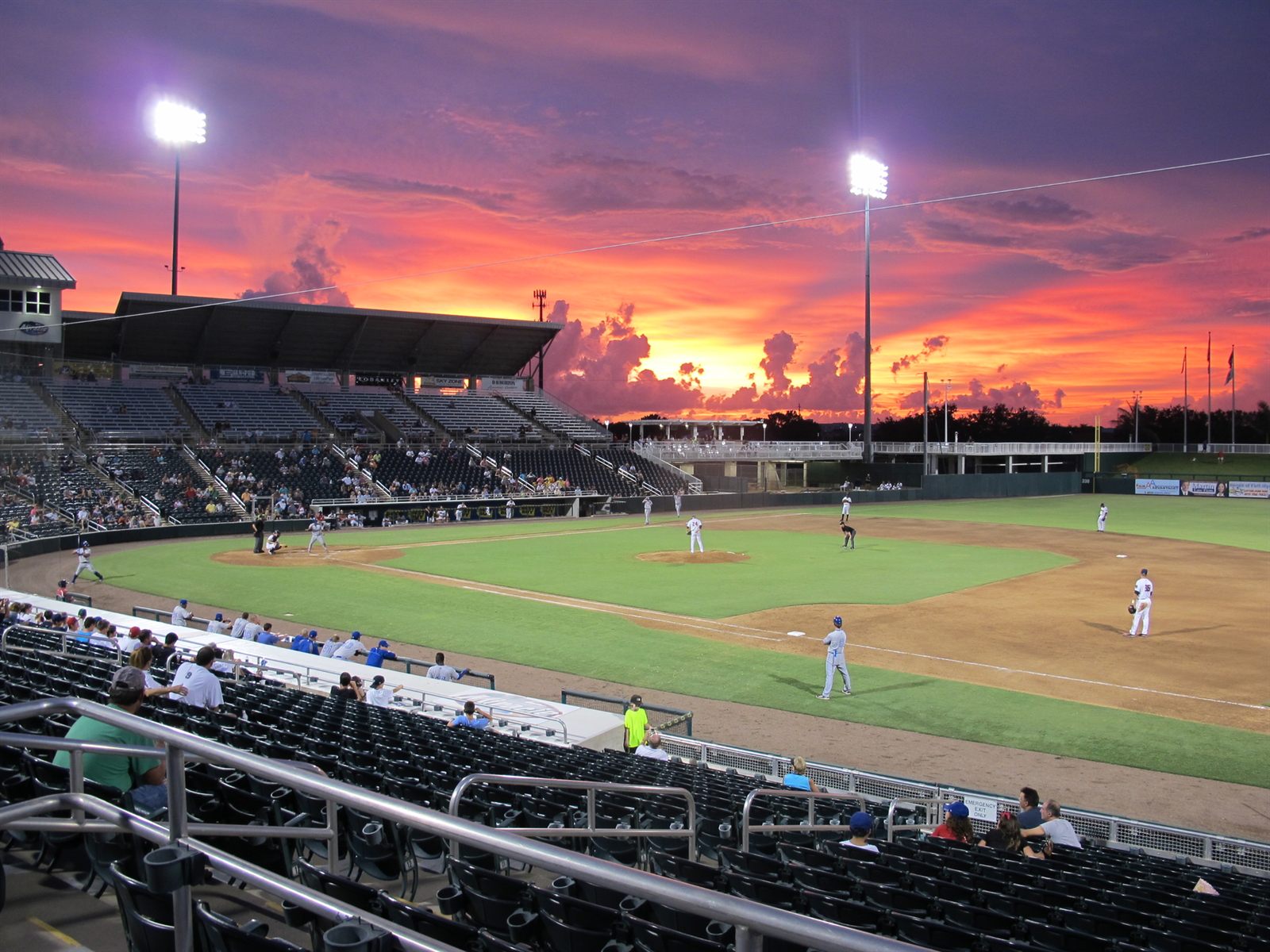 A minor league baseball game under the lights as the sky turns pink and orange at sunset