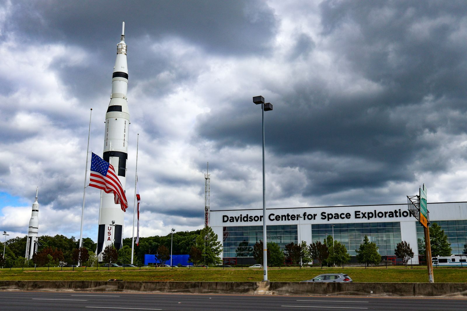 The Saturn V rocket replica standing beside the Davidson Center for Space Exploration at the U.S. Space and Rocket Center in Huntsville, under storm clouds